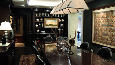Dark-panelled dining room with a long table, black chairs, a pendant light and a framed textile on the wall