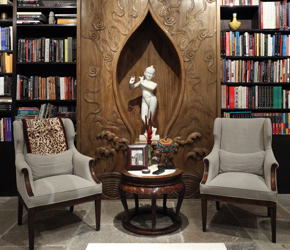 Library entrance with a carved wooden niche and white figure, two grey armchairs and floor-to-ceiling bookshelves