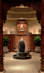 A stone lingam on a low pedestal framed by carved Indian arches and potted palms