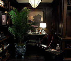 Dark-panelled Ralph Lauren Home study with a potted palm in a blue-and-white planter, a landscape painting and a desk lamp